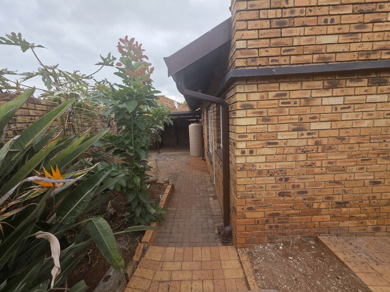A side view of the townhouse exterior featuring face brick walls, a paved walkway, and a water storage tank in the rear garden area.