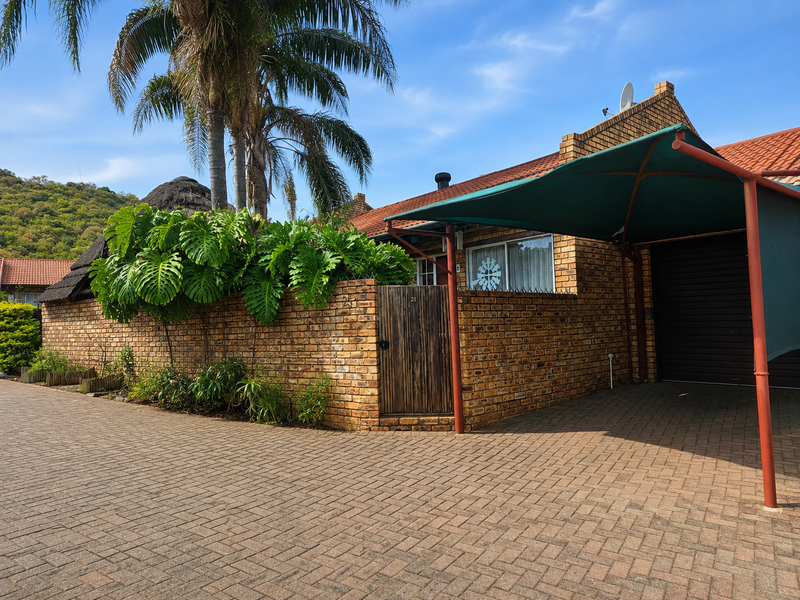 Front exterior view of a townhouse featuring a face brick facade, paved driveway, and a covered shade cloth carport.