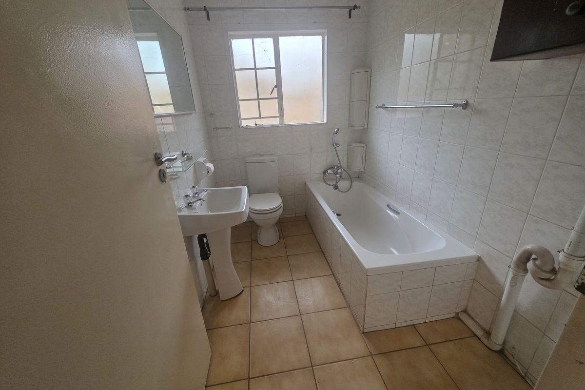 A functional bathroom featuring a pedestal basin, toilet, and bathtub with tiled finishes. The space is ready for modernization and cosmetic updates.