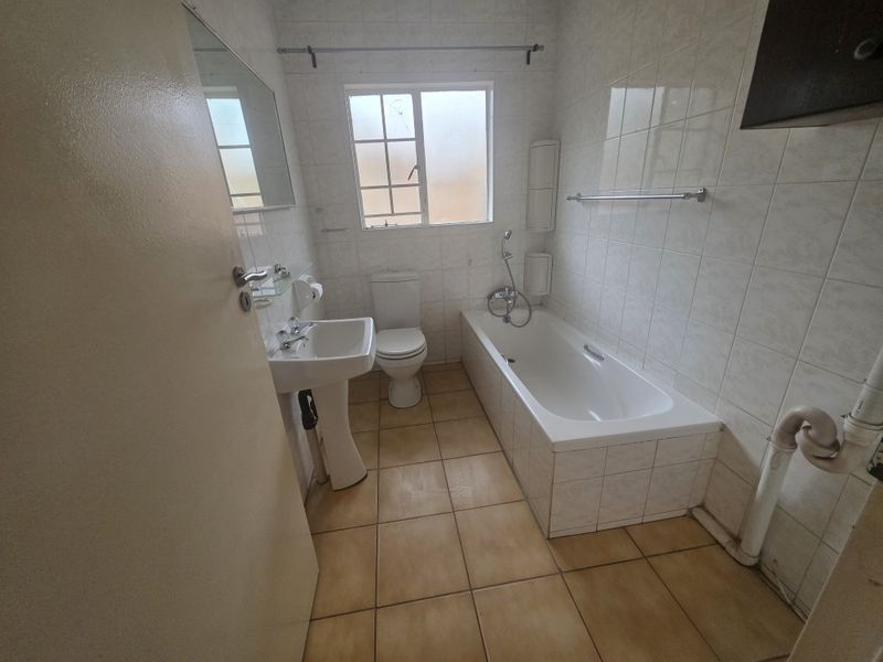 A functional bathroom featuring a pedestal basin, toilet, and bathtub with tiled finishes. The space is ready for modernization and cosmetic updates.
