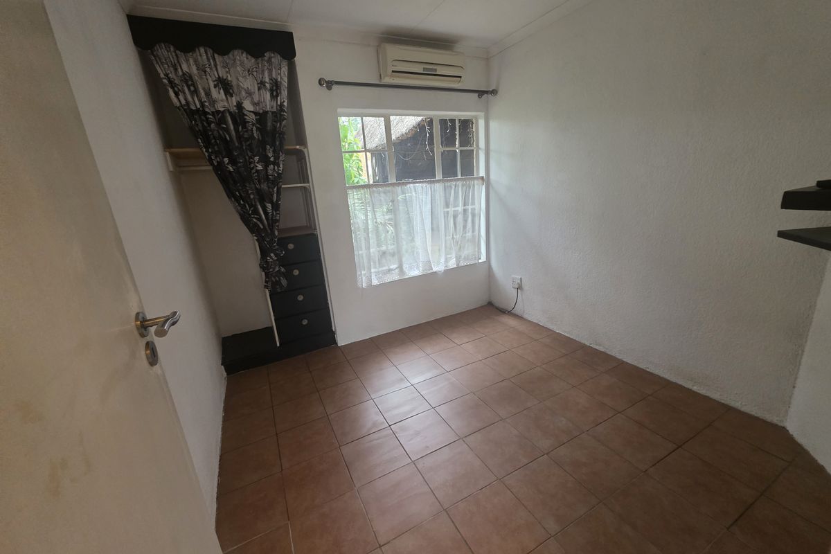 A compact bedroom featuring tiled flooring, a built-in cupboard, and a wall-mounted air conditioning unit.