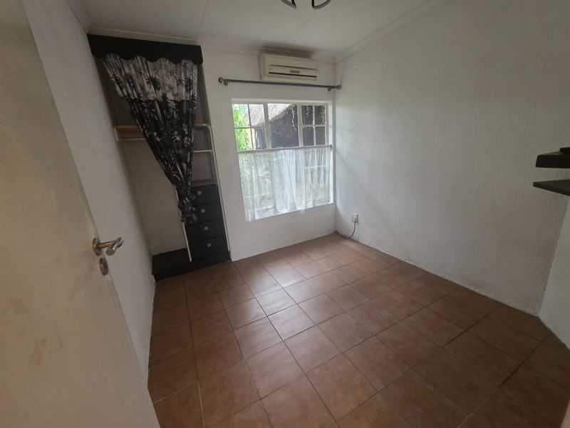A compact bedroom featuring tiled flooring, a built-in cupboard, and a wall-mounted air conditioning unit.