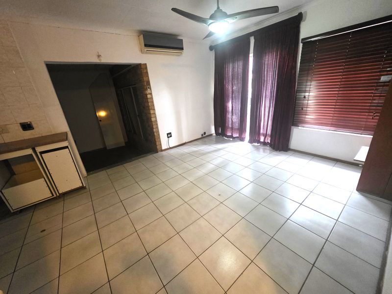 Open plan living area featuring tiled flooring, a ceiling fan, split-system air conditioning, and built-in cabinetry with some missing doors.