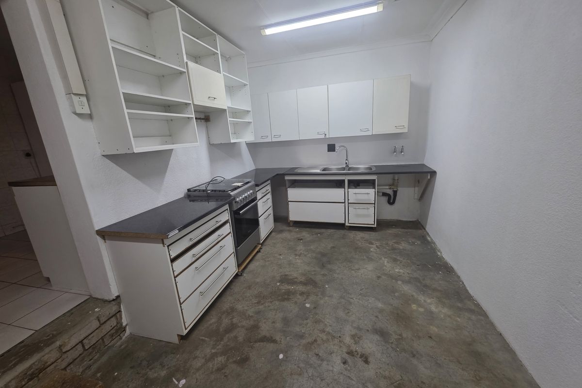 A basic, unfinished kitchen area featuring built-in cabinetry, a stainless steel sink, and a freestanding stove, requiring flooring and cosmetic updates.