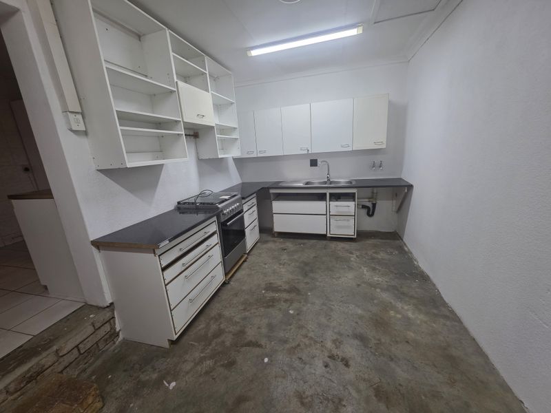 A basic, unfinished kitchen area featuring built-in cabinetry, a stainless steel sink, and a freestanding stove, requiring flooring and cosmetic updates.