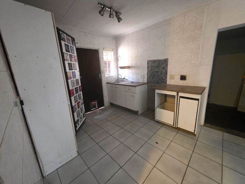A functional scullery or utility area featuring tiled flooring, a sink, and built-in cabinetry, currently requiring cosmetic updates and cabinet repairs.