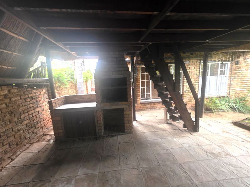 Covered outdoor patio area featuring a built-in brick braai, tiled flooring, and a timber staircase leading to an upper level.