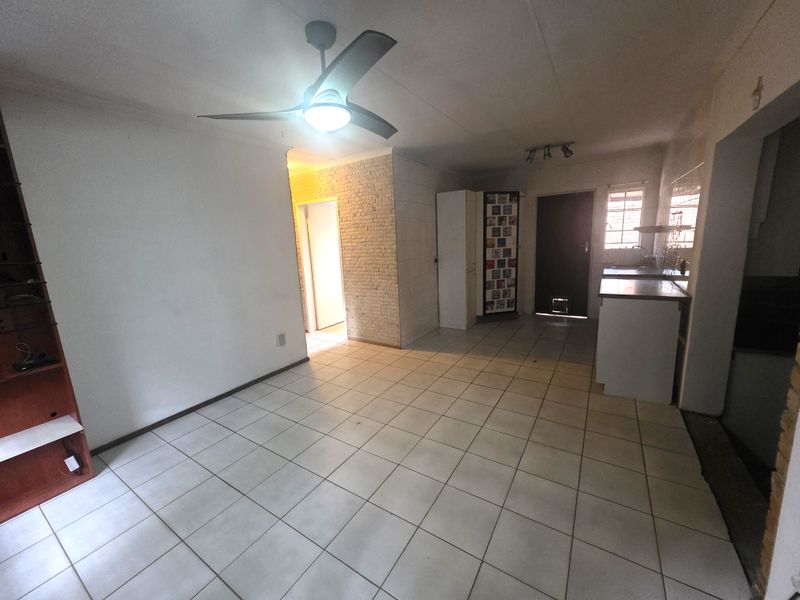 Open-plan living and kitchen area featuring tiled flooring, a ceiling fan, and a textured brick feature wall, offering a blank canvas for renovation.