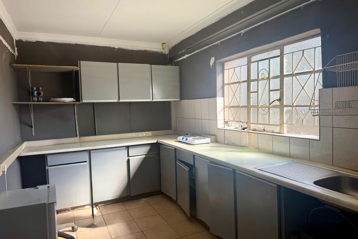 A dated kitchen featuring built-in cabinetry, tiled backsplash, and a stainless steel sink, requiring renovation to modernize the space.