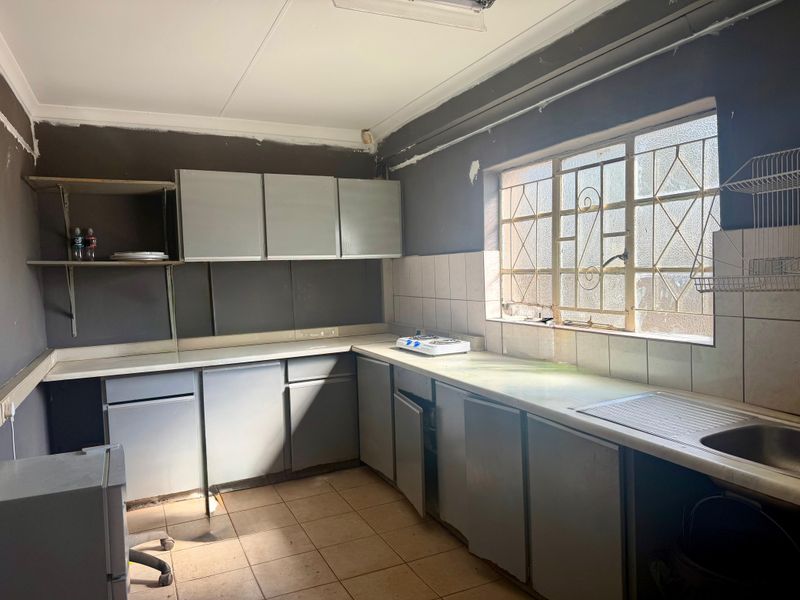 A dated kitchen featuring built-in cabinetry, tiled backsplash, and a stainless steel sink, requiring renovation to modernize the space.