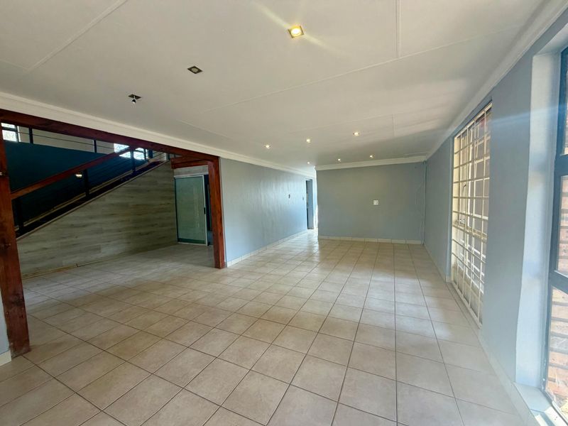 Spacious, open-plan living area featuring neutral tiled flooring, recessed lighting, and a timber staircase leading to the upper level.
