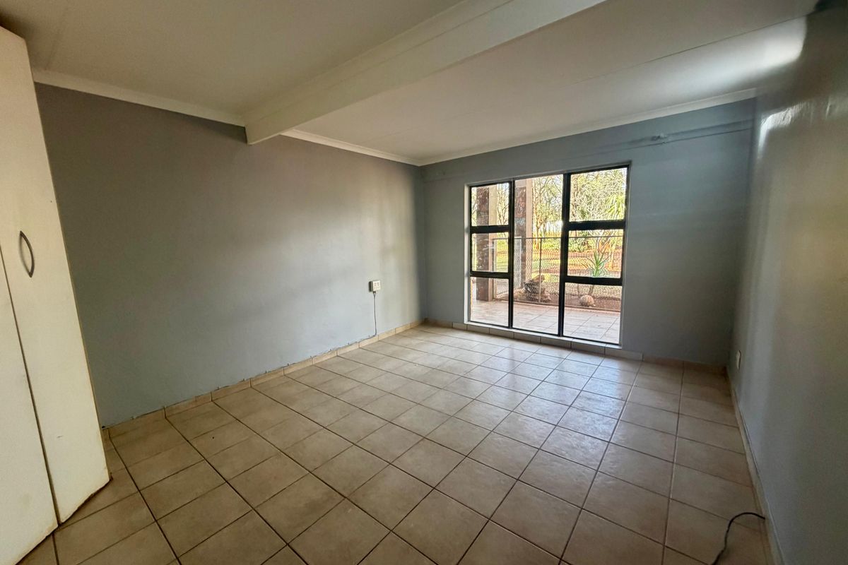 A vacant bedroom featuring tiled flooring, a built-in cupboard, and large aluminium-framed windows providing natural light and garden views.