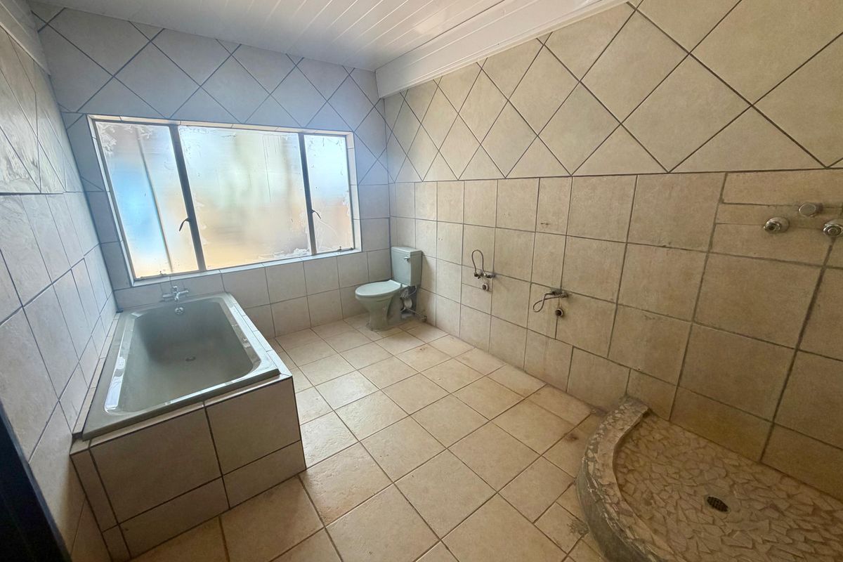 Spacious bathroom featuring a built-in bathtub, toilet, and a tiled shower base. The room is currently vacant and requires cosmetic updates.