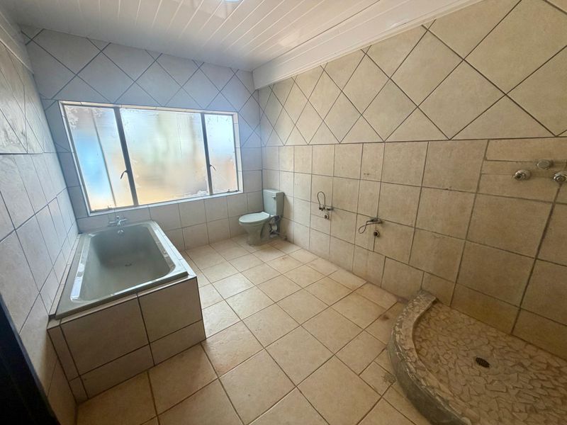 Spacious bathroom featuring a built-in bathtub, toilet, and a tiled shower base. The room is currently vacant and requires cosmetic updates.