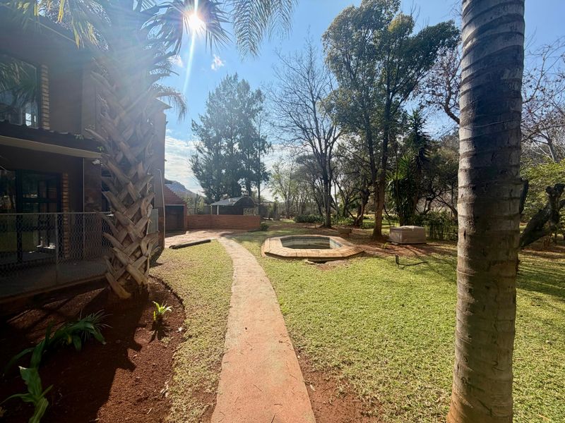 Spacious rear garden featuring a paved walkway, mature trees, and an existing swimming pool area.