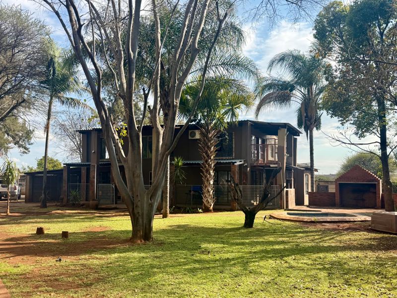 Rear view of a two-story house featuring a spacious garden, a swimming pool, and a built-in brick braai area.