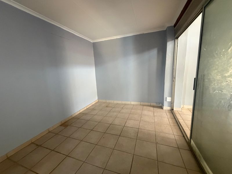 An empty living area featuring ceramic floor tiles, coved ceiling cornices, and a sliding glass door providing access to an outdoor space.