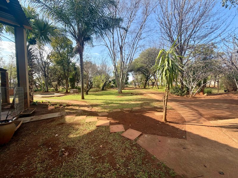 A spacious, well-established garden featuring mature trees, a paved walkway, and a large lawn area, offering a peaceful outdoor setting.