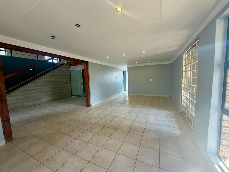 Spacious, empty living area featuring tiled flooring, recessed lighting, and a prominent timber-framed staircase, offering a versatile open-plan layout.