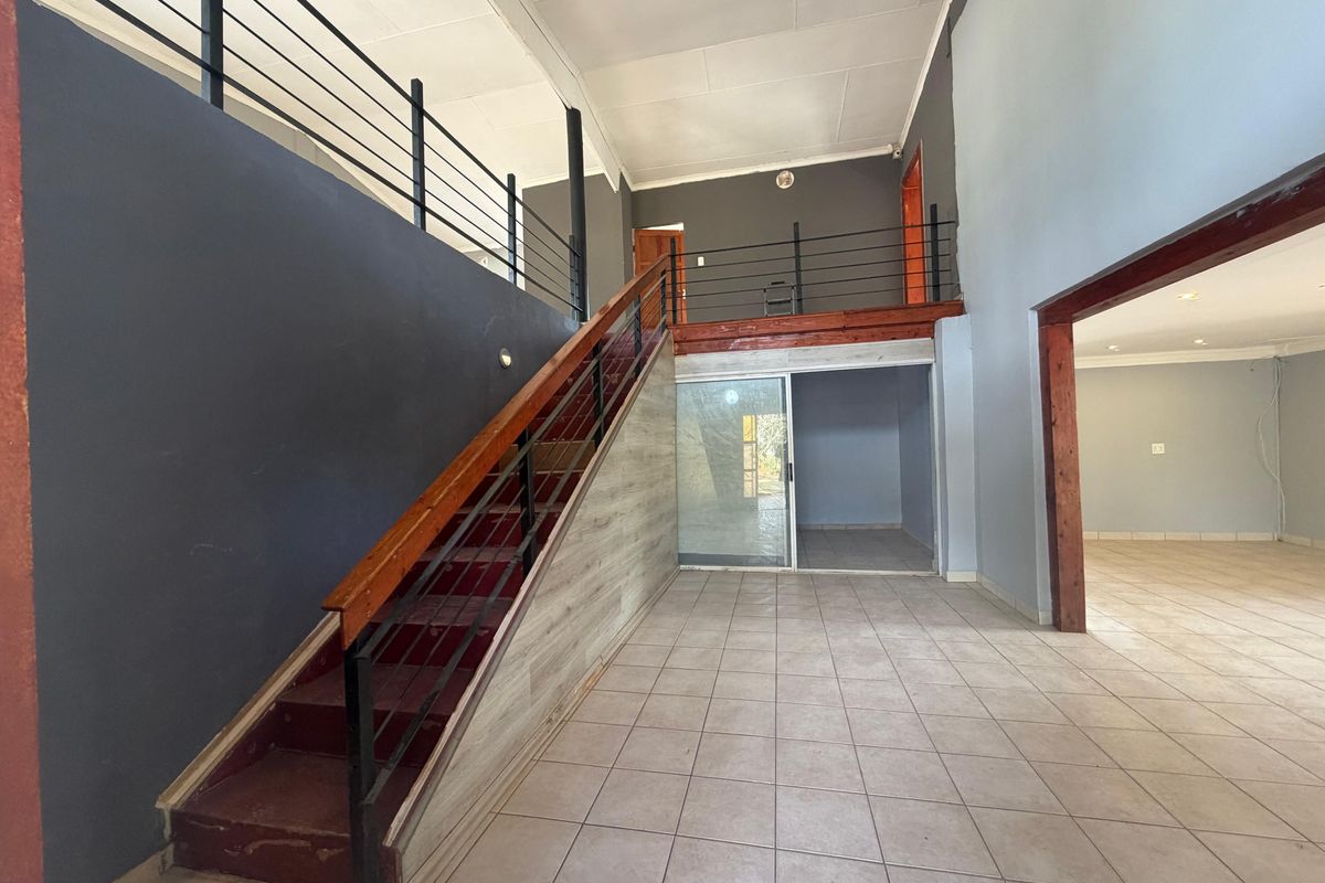 Spacious open-plan living area featuring a prominent staircase leading to a mezzanine level, tiled flooring, and neutral wall finishes.