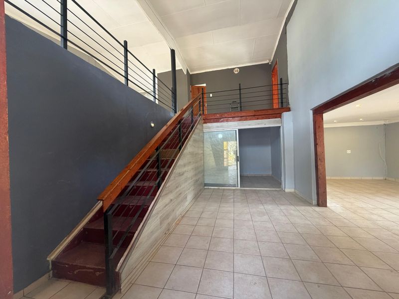 Spacious open-plan living area featuring a prominent staircase leading to a mezzanine level, tiled flooring, and neutral wall finishes.