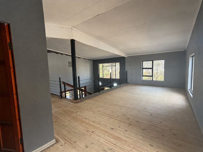 An expansive, empty upper-level living area featuring polished timber flooring, a metal balustrade overlooking the lower level, and large windows providing natural light.