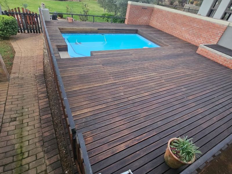 Outdoor pool area featuring a timber deck surround, brick retaining wall, and adjacent brick pathway, overlooking a garden space.