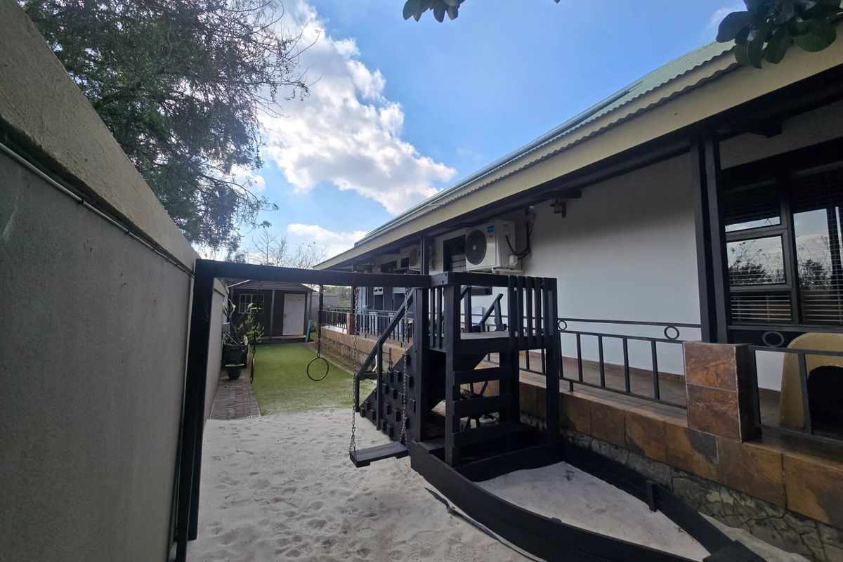 Rear exterior view featuring a covered patio with metal railings, stone cladding accents, and a landscaped garden area with a play structure.