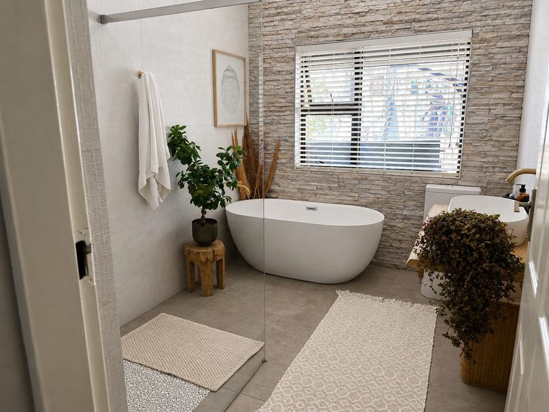 Modern bathroom featuring a freestanding bathtub, stone feature wall, glass shower screen, and a stylish vessel sink on a wooden vanity.