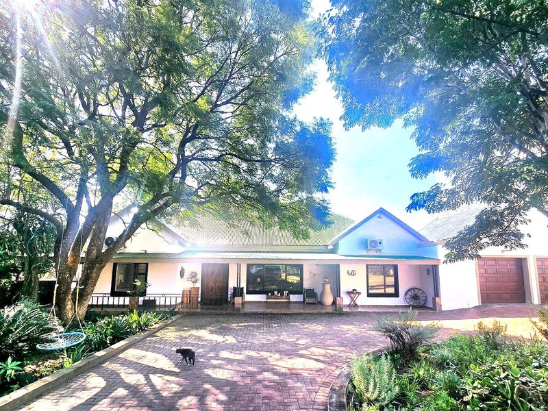 Front view of a single-story house featuring a paved driveway, covered porch, and an attached double garage surrounded by mature trees.