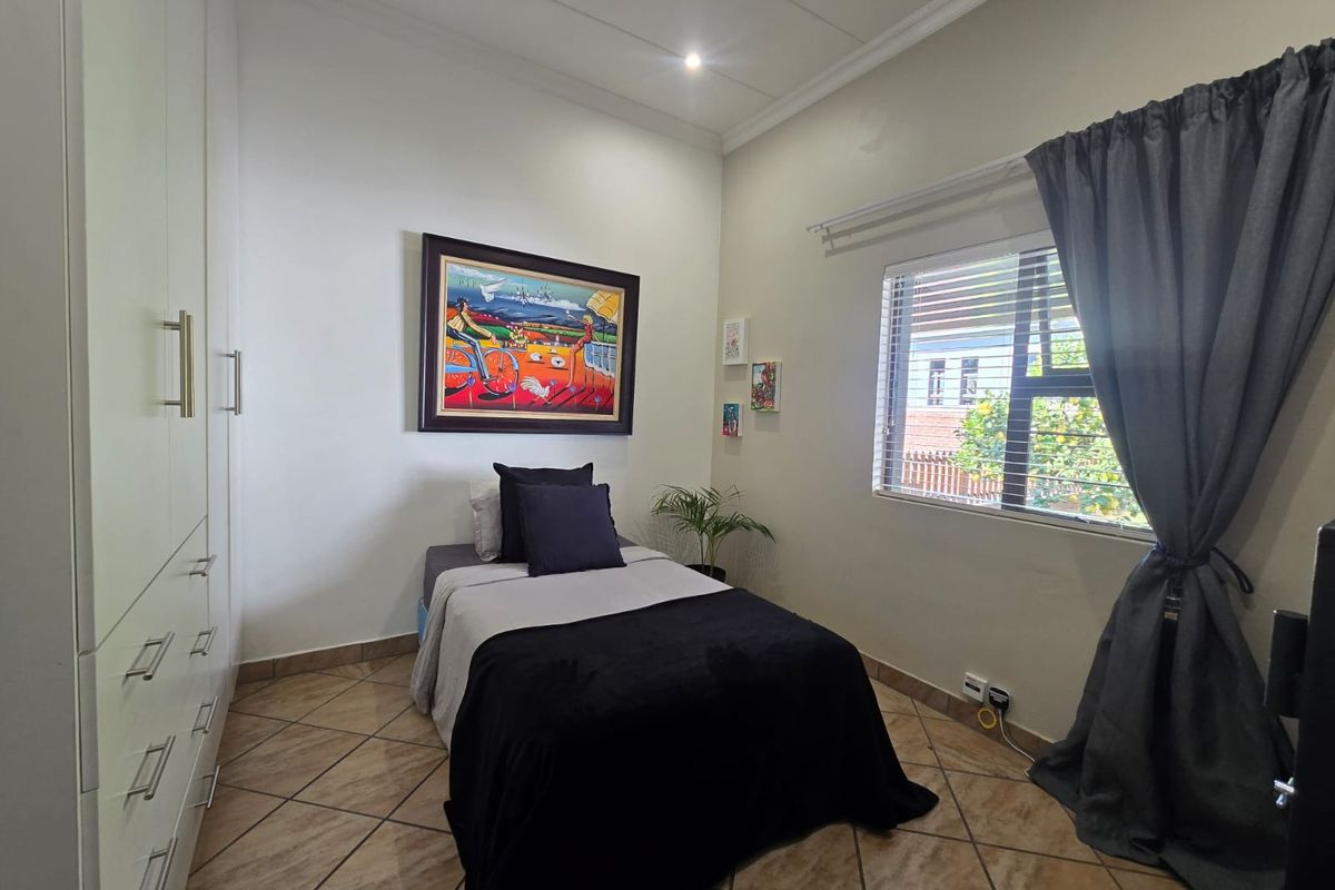 A well-maintained bedroom featuring built-in cupboards, tiled flooring, and a window with blinds, offering a clean and functional living space.