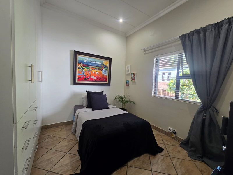 A well-maintained bedroom featuring built-in cupboards, tiled flooring, and a window with blinds, offering a clean and functional living space.