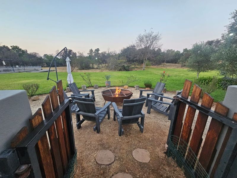 A well-maintained outdoor garden area featuring a central fire pit, gravel flooring, and timber fencing overlooking a spacious lawn.