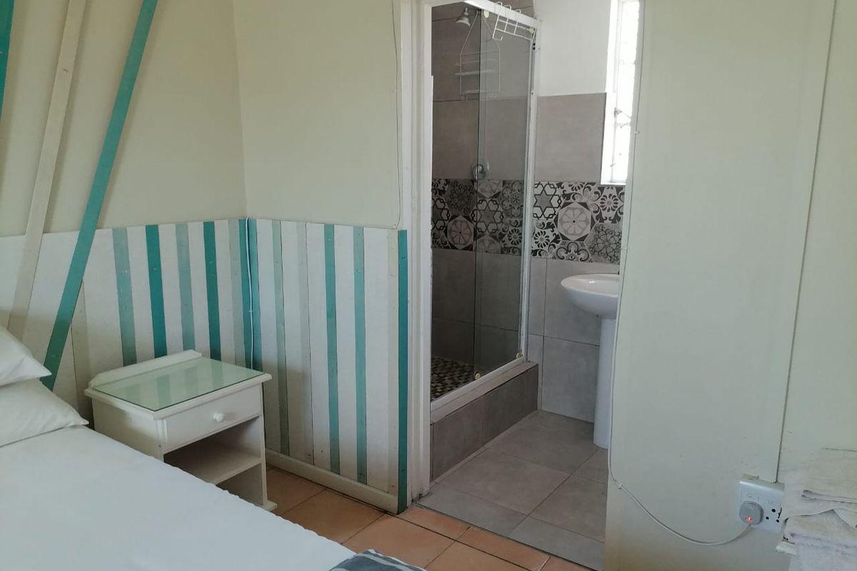 A bedroom featuring an en-suite bathroom with a glass shower enclosure and pedestal basin, finished with tiled flooring and decorative wall paneling.
