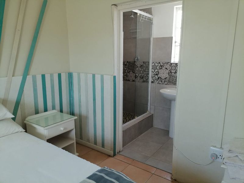A bedroom featuring an en-suite bathroom with a glass shower enclosure and pedestal basin, finished with tiled flooring and decorative wall paneling.