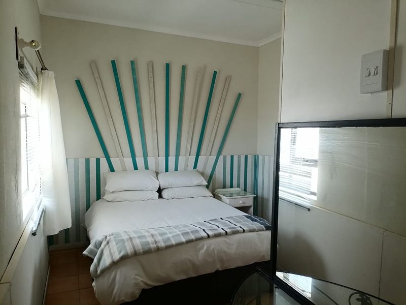 A compact bedroom featuring tiled flooring, a built-in cupboard, and window blinds, offering a functional living space.