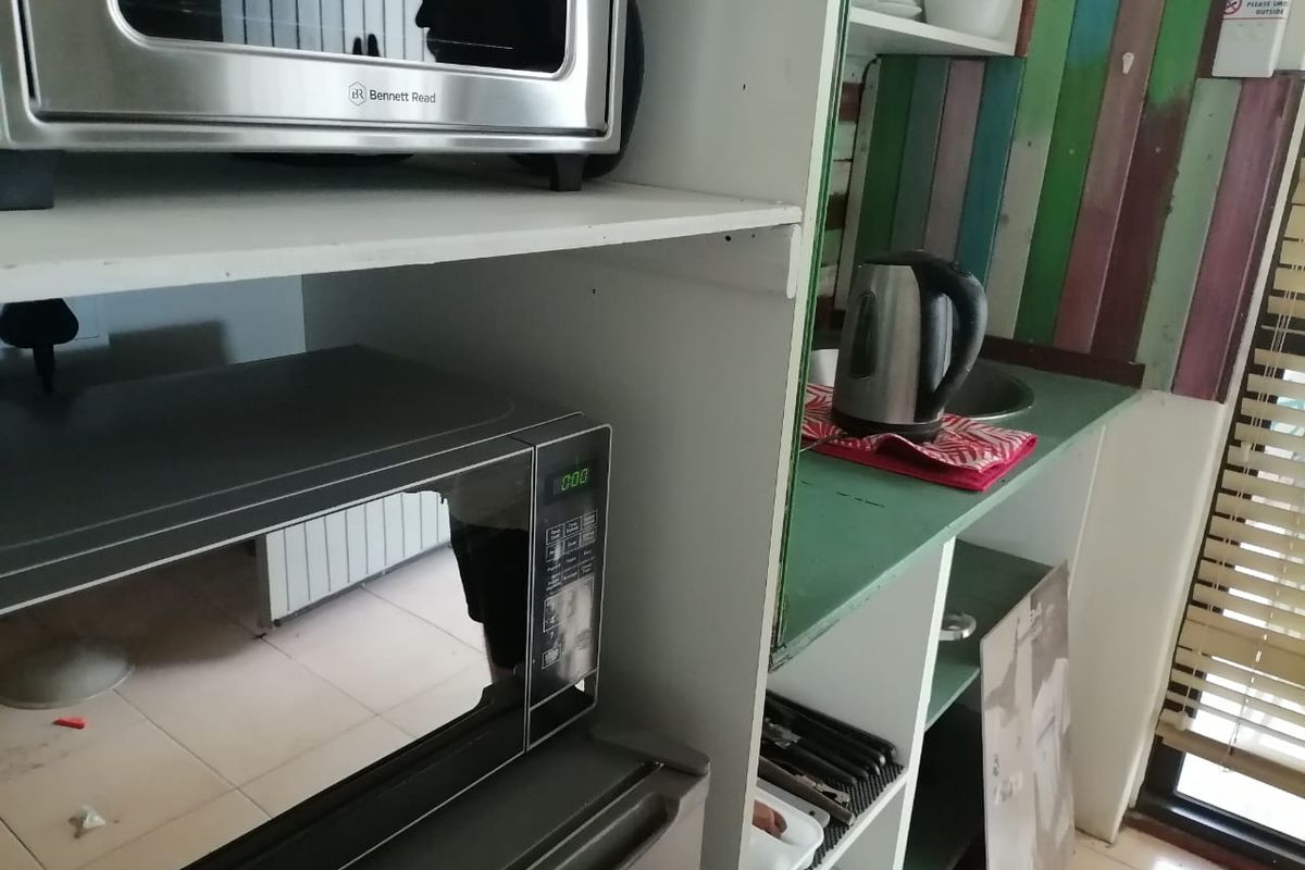 A compact kitchen area featuring built-in shelving, a small sink, and tiled flooring, currently showing signs of wear and dated finishes.