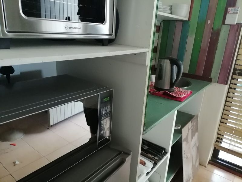 A compact kitchen area featuring built-in shelving, a small sink, and tiled flooring, currently showing signs of wear and dated finishes.