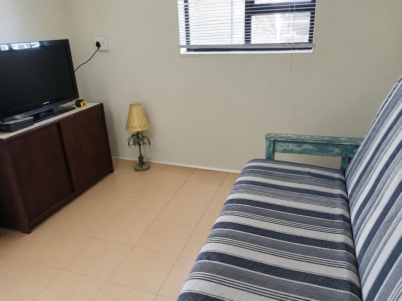 A simple living room area featuring neutral tiled flooring, a window with venetian blinds, and standard electrical fixtures.