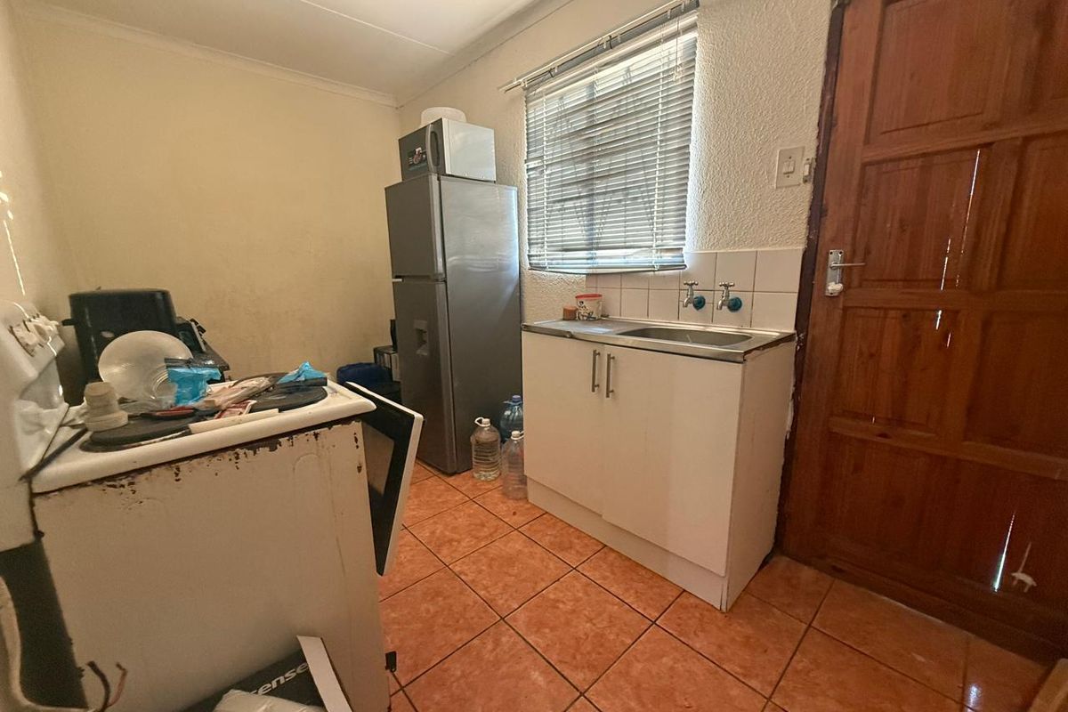 Compact kitchen area featuring tiled flooring, a stainless steel sink, built-in cabinetry, and direct access via a timber door.