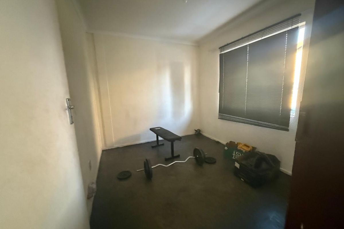 A simple, empty bedroom featuring dark flooring and fitted venetian blinds, offering a blank canvas for potential renovation or restyling.