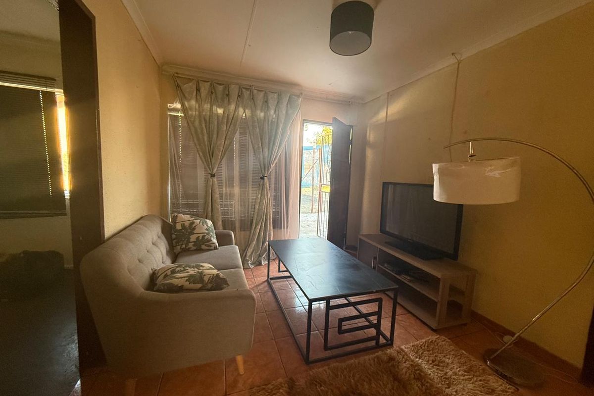 A compact living room featuring tiled flooring and direct access to an outdoor area, providing a functional space with potential for cosmetic updates.
