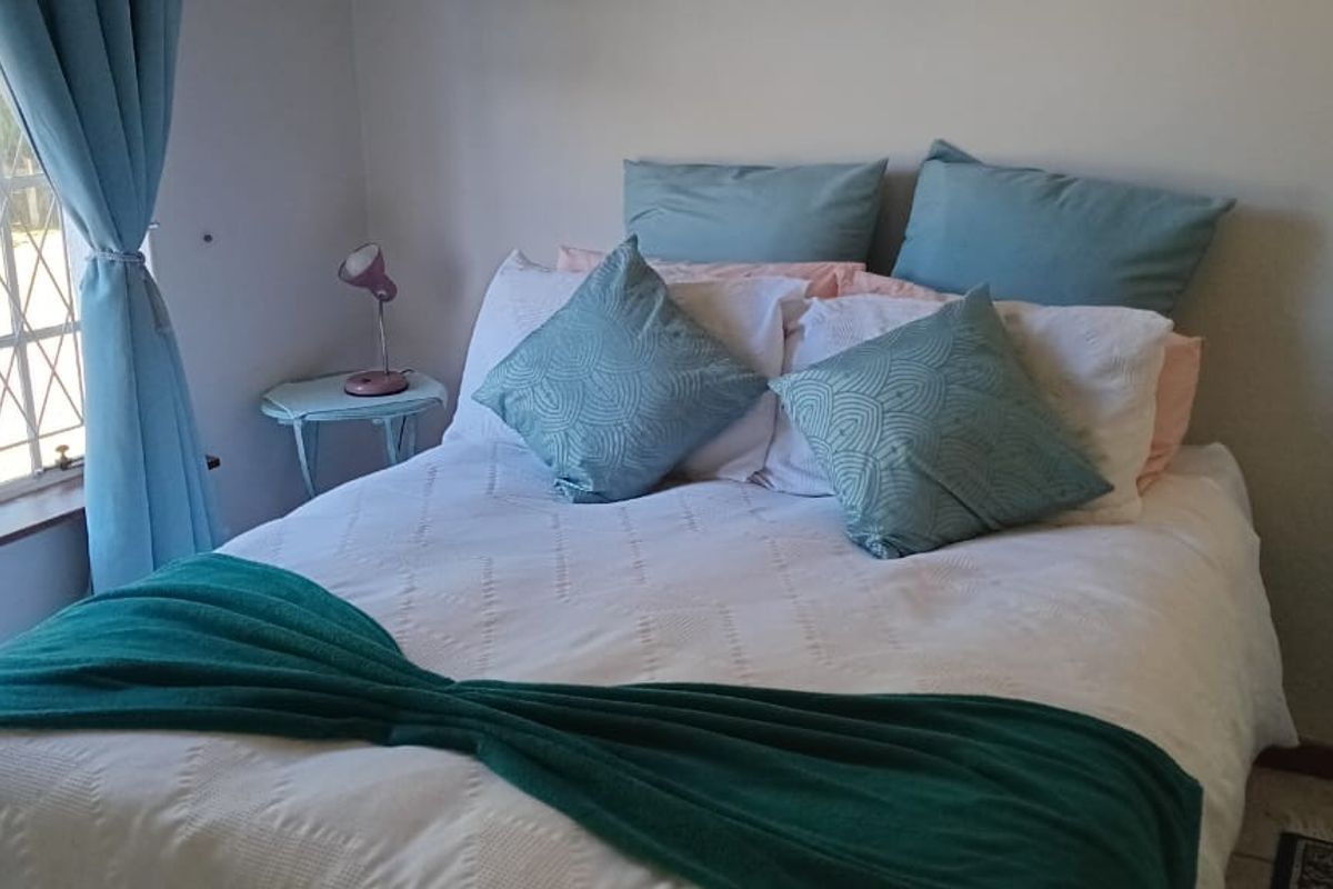 A cozy bedroom featuring tiled flooring and a large window with security bars, providing natural light.