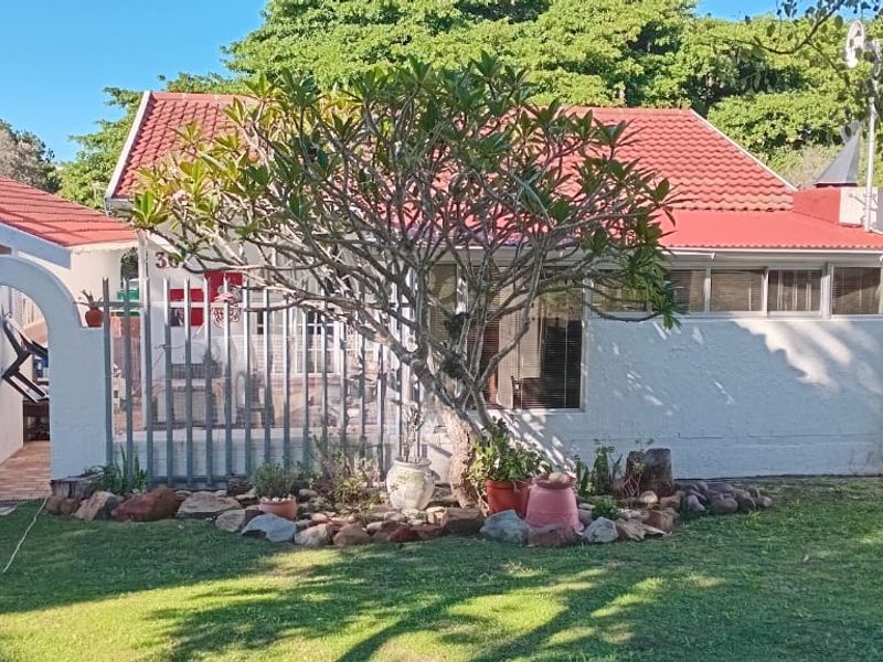 Rear view of the townhouse featuring a tiled roof, plastered exterior walls, and a secure gated entrance leading to a paved walkway.