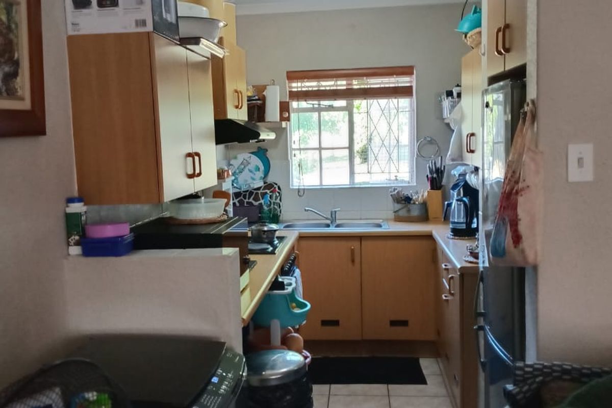 A functional kitchen featuring laminate cabinetry, a double basin sink, and a built-in hob with an extractor fan, finished with tiled flooring.