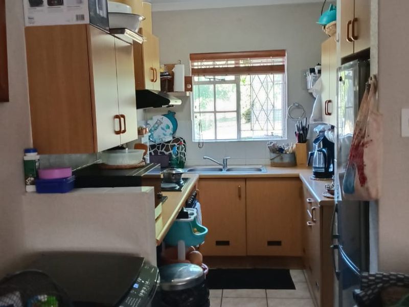 A functional kitchen featuring laminate cabinetry, a double basin sink, and a built-in hob with an extractor fan, finished with tiled flooring.