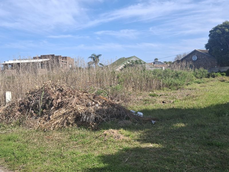 A vacant residential plot featuring overgrown grass and a pile of garden debris, situated in a developed neighborhood.