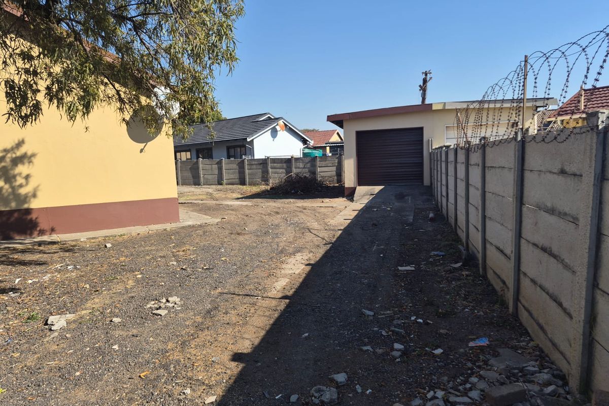 Rear exterior view showing a gravel driveway, a single garage, and a precast concrete boundary wall topped with razor wire.