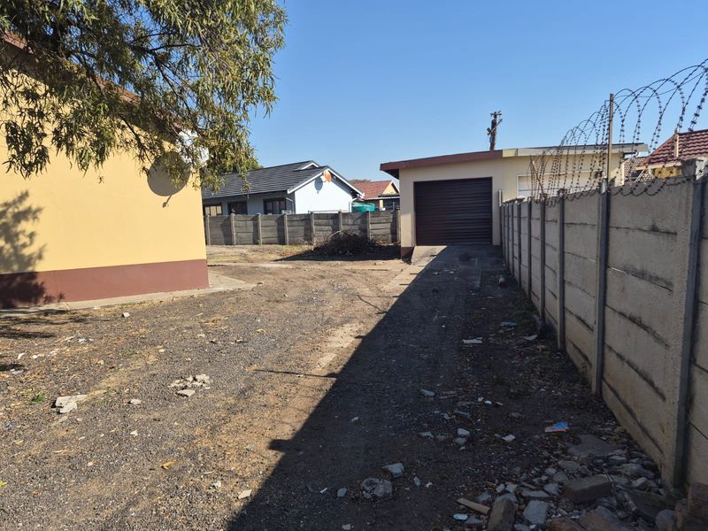 Rear exterior view showing a gravel driveway, a single garage, and a precast concrete boundary wall topped with razor wire.