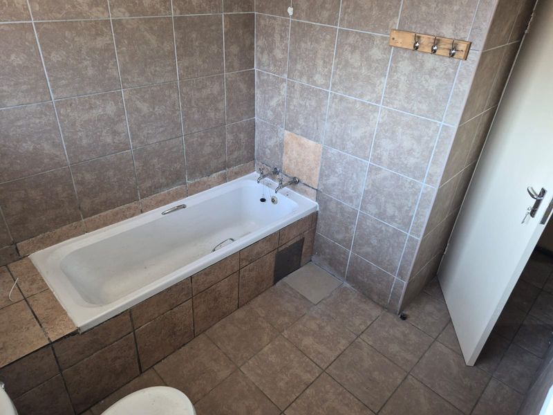 A dated bathroom featuring a built-in bathtub with tiled surround and flooring, requiring cosmetic updates and repairs to the tiling.